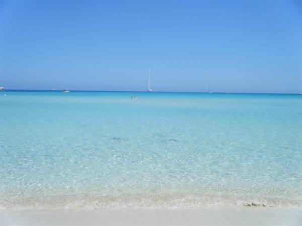 Clear turquoise water over white sand, sailboats on the horizon