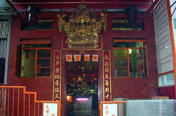 Chinese temple with red tiled facade, golden inscriptions and gilded ornament above entrance
