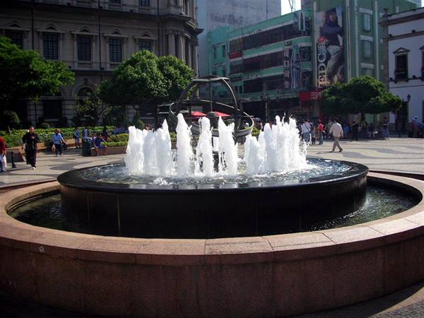 Stone fountain with water jets and armillary sphere, square with pedestrians, Macao