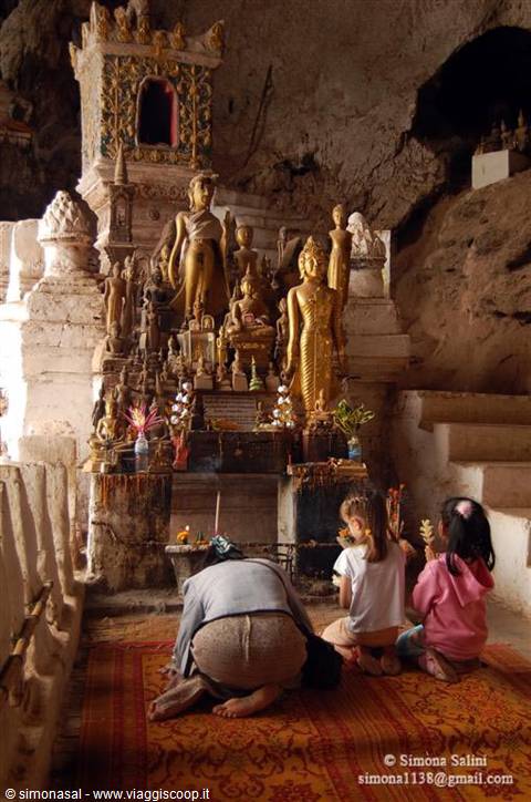 Women kneel praying before golden Buddha statues inside Pak Ou cave