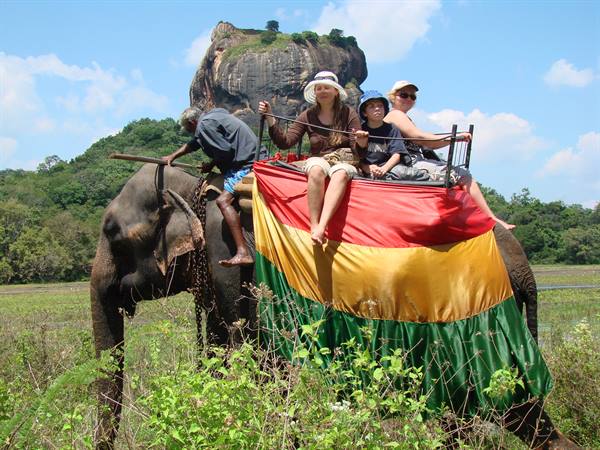 Tourists riding a draped elephant with Sigiriya rock rising behind