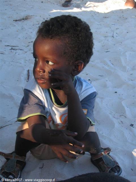 Child sitting on white sand touching his face with one hand