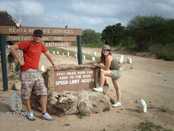 Tourists crouching by the entrance sign at Tsavo East National Park