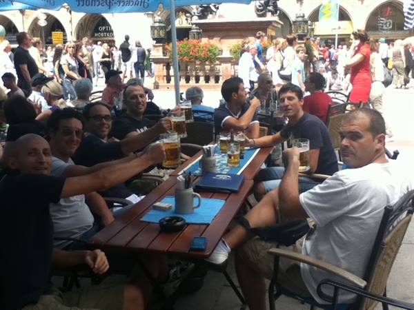 Friends toasting with beers at an outdoor bistro table in a busy square