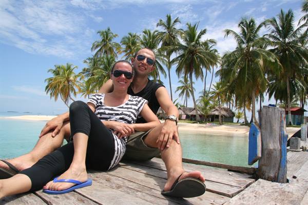 Couple in sunglasses sitting on wooden dock among palms and huts