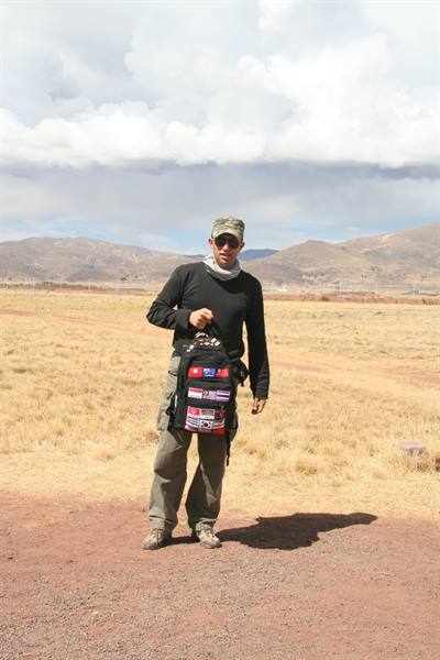 Man in cap holding a backpack covered with flags on dry plain