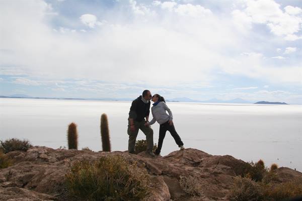 Couple kissing on rocks among cacti, Isla Incahuasi, white salt flat below