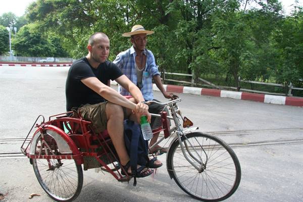 Tourist on a red cycle rickshaw, driver pedaling in straw hat