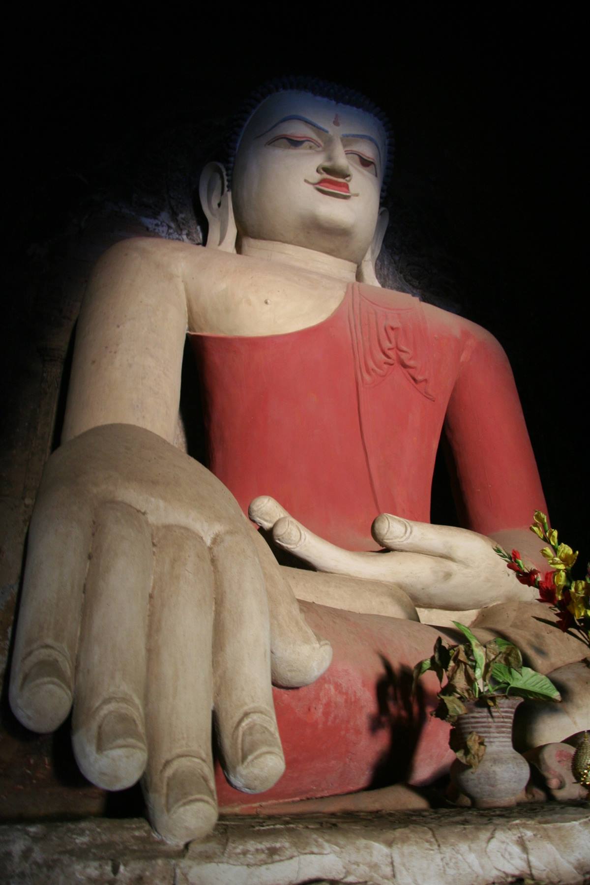 Grande statua di Buddha seduto, veste rossa, mano enorme in primo piano, luce laterale
