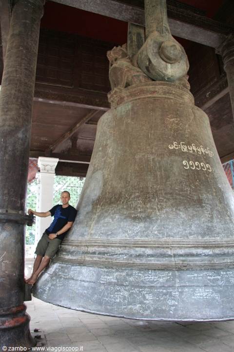 Tourist leaning against the giant Mingun Bell under the wooden pavilion