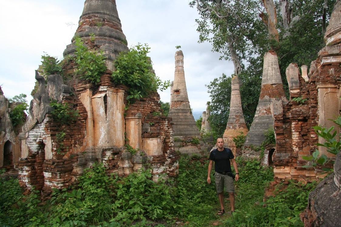 Uomo tra vecchi stupa in mattoni invasi dalla vegetazione a Shwe Inn Dein