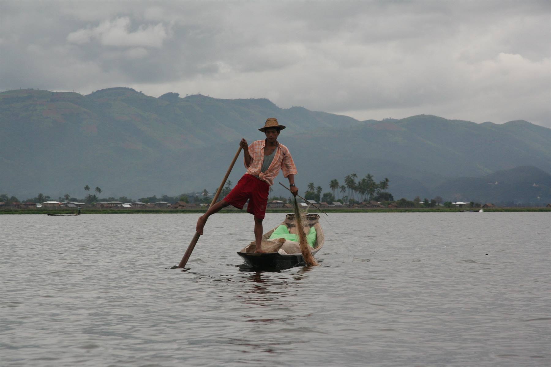 Pescatore rema con una gamba sulla piroga nel lago Inle