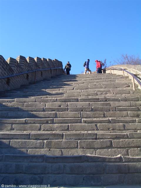 Tourists climb the steep stone steps of the Great Wall under blue sky