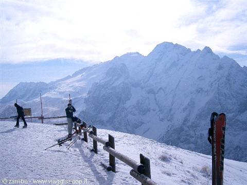 Skiers with skis beside a wooden fence, snowy peaks and mist