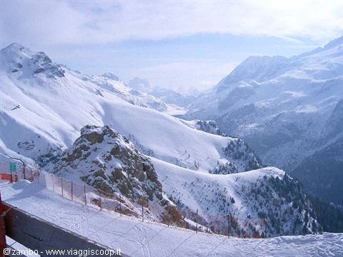 Snowy ski slopes among rocks and mountains under cloudy sky