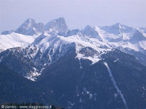 Snow-capped Dolomite peaks under clear sky, dark forests below