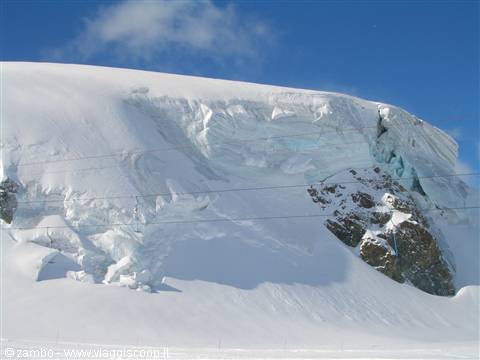 Snow-covered glacier with blue crevasses and ski lift cables, clear sky