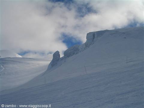 Old poles emerge from snow beneath icy formations and cloudy sky