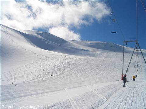 Ski lift over snowy glacier, skiers climb between fresh snow and cloudy sky