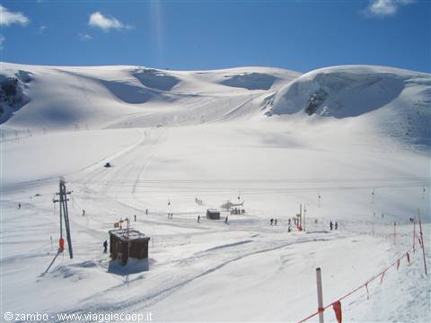 Skiers on a snowy glacier with ski lift poles and wooden huts