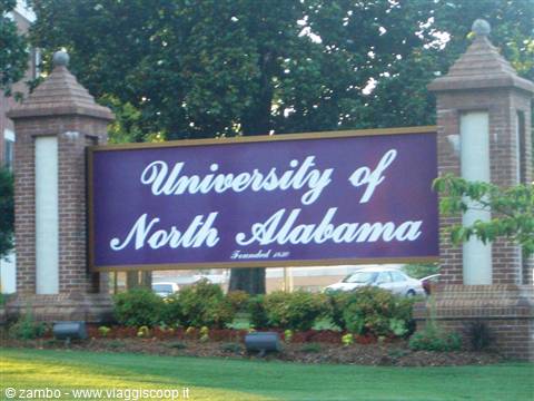 Purple University of North Alabama sign between brick pillars, flower garden