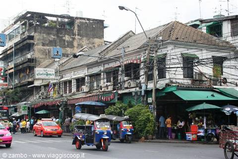 Tuk-tuks and taxis parked outside old shophouses on a busy Bangkok street