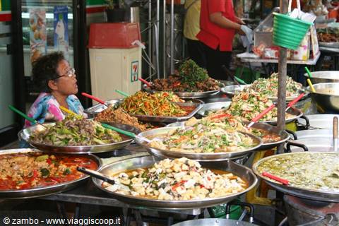 Woman seated among large trays of Thai street food at a market