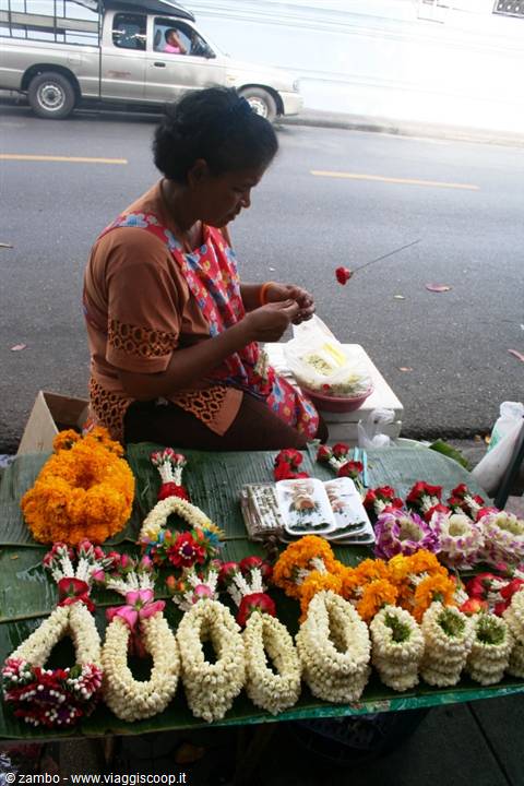 Woman assembles flower garlands of jasmine and marigolds on banana leaves