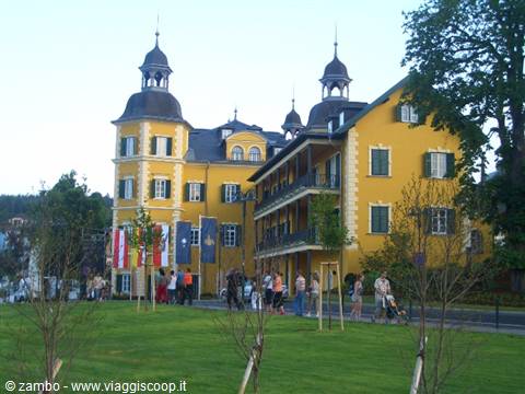 Yellow palace with green towers in Bad Ischl, tourists along the tree-lined path