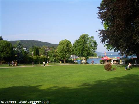 Green lawn by Lake Wörthersee, trees, people and hills in sunshine