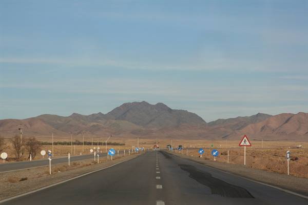 Iranian desert highway toward mountains, blue road signs along the asphalt