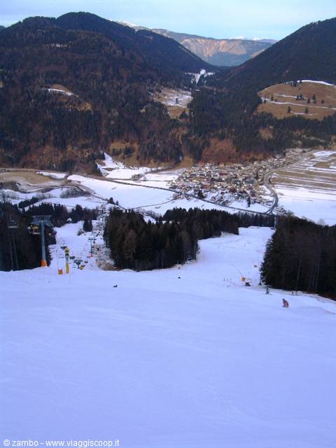 Snowy ski slope with chairlift and skier, village in valley among woods