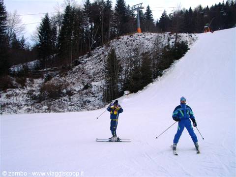Two skiers in blue and yellow suits skiing downhill beneath the chairlift