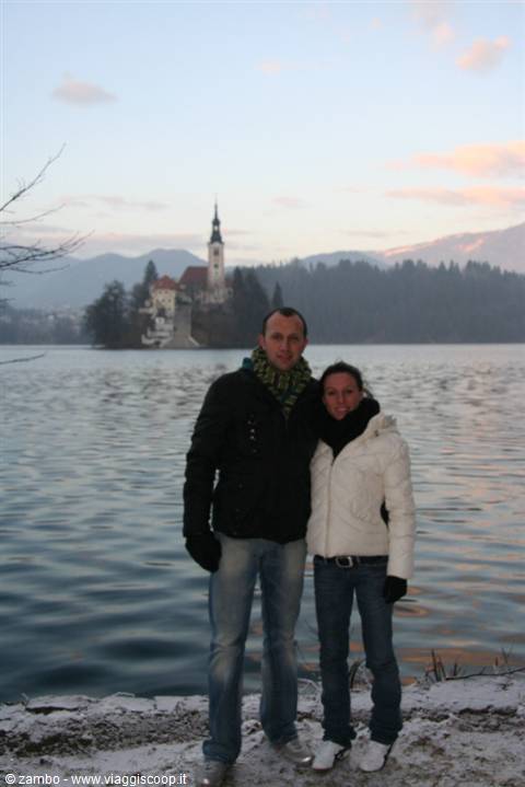 Couple on the snowy shore of Lake Bled with the island church behind