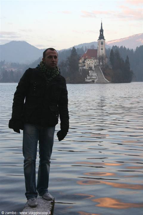 Traveler standing on a pillar in Lake Bled, island church behind him
