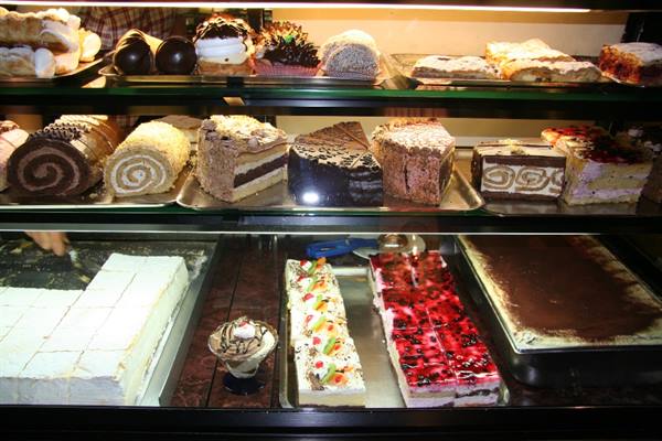 Pastry shop display case with cakes, rolls and desserts under warm light