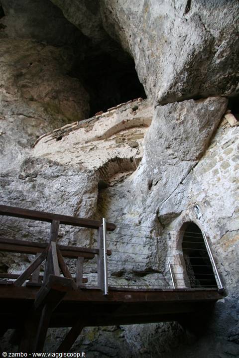 Wooden walkway with metal railing in front of rock cave with stone walls