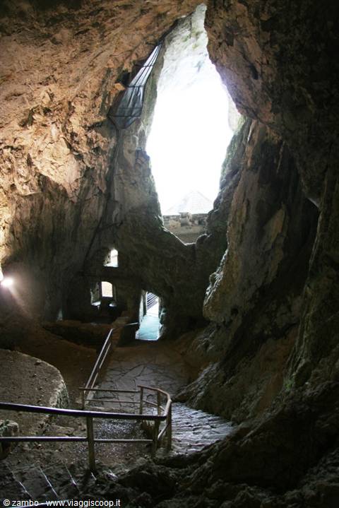 Stone staircase inside a cave, daylight pouring through a huge rock opening