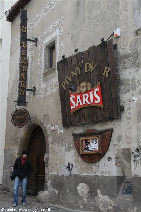 Wooden sign of Pivný Dvor Šariš pub on old facade, man walking by