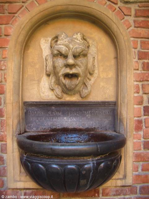 Stone fountain with grotesque mask and black basin set in brick wall