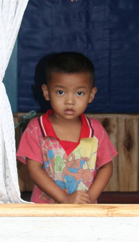 Boy in pink Spider-Man shirt at the wooden window of a house