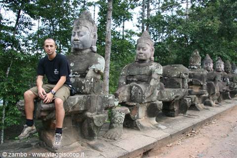 Tourist sitting among the stone deva statues on the causeway of Angkor Thom