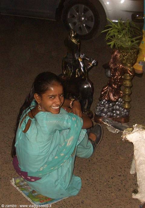 Girl in turquoise sari sitting beside brass Krishna statues at night