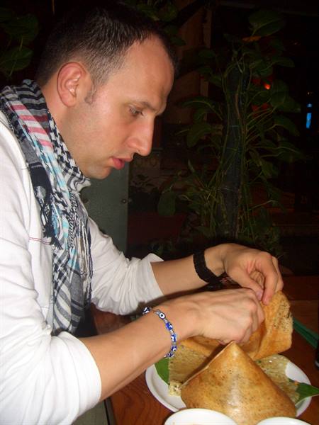 Man in checkered scarf tears a dosa at a dim restaurant