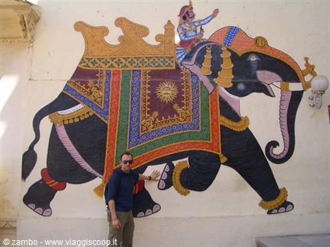 Tourist posing next to a mural of a decorated elephant with colorful traditional saddles