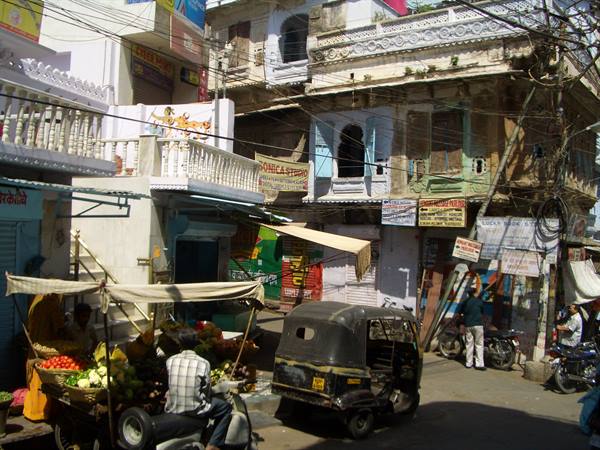 Indian street market: vegetable cart, auto rickshaw and old haveli buildings