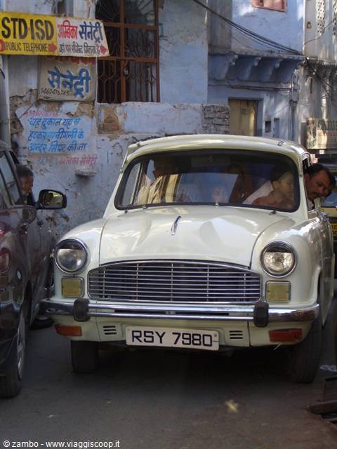 Old white Ambassador car in an alley with Hindi signs