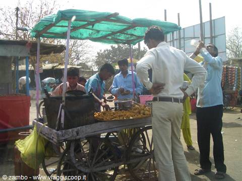 Street food vendor at a wooden cart under green canopy, customers buying snacks