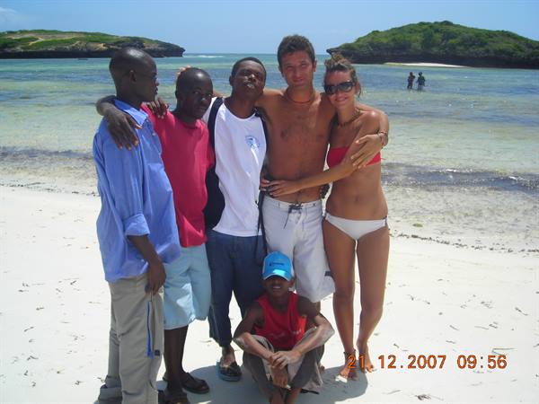 Friends hugging on white sand beach, a boy crouching in front