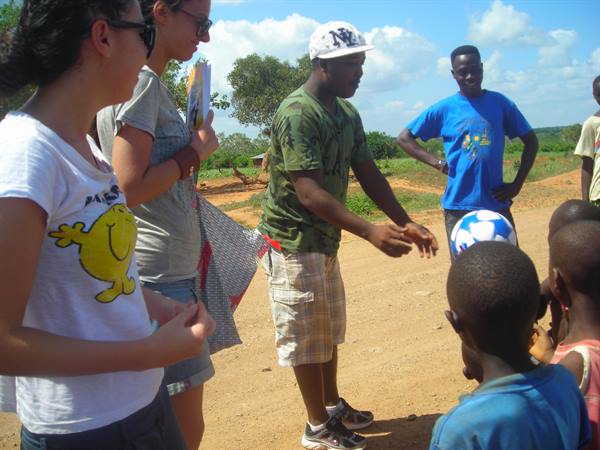 Tourists and local kids play with a soccer ball on a dirt road